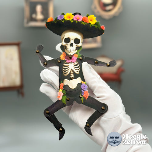 Calacas, a printable articulated paper doll. A skeleton in a black sombrero trimmed with flowers.